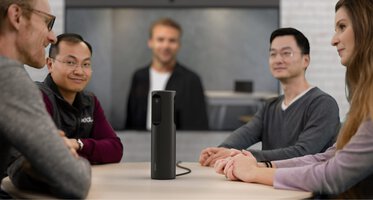Konferenzraum mit der Neat Center in der Mitte eines Konferenztisches, mehrere Personen sitzen darum und haben ein Meeting