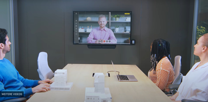 Konferenzraum mit drei Personen, frontseitig hängt ein Display, darunter die Videobar 